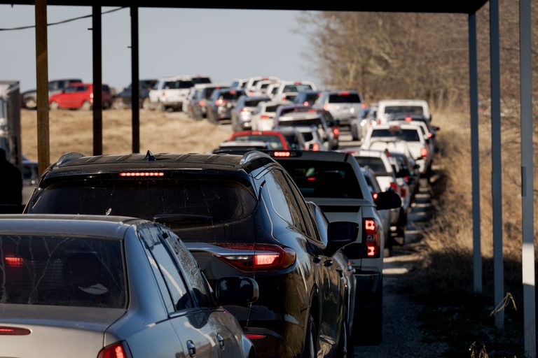 A long line of cars and pickup trucks waiting on a dirt track at the food bank.