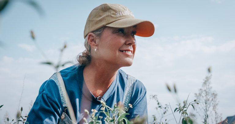 Dr. Leanna Brewer outdoors in a field, in a cap and work shirt, looking into the distance.